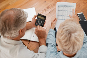 An elderly couple reviewing financial documents together in a bright living room, smiling and relaxed.